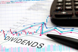 DIVIDENDS text on documents with graphs, charts, calculator, pen, financial concept background.