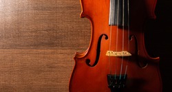 Violin, details of a beautiful violin on wooden surface and black background, low key selective focus portrait.