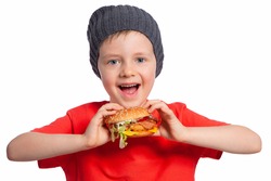 A child eats a cheeseburger. The boy looks at the Burger with an appetite. A beautiful European boy is going to eat fast food. Happy child. A hamburger snack. Favorite children's food.