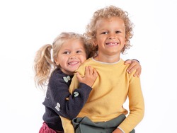 Portrait of a 4-and 3-year-old brother and sister. Beautiful European children on a white background, close-up. A boy and a girl hug and laugh. The children are tanned and curly-haired.