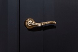 Stylish gold handle on a black door. Modern trends in interior design. Close-up.
