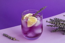 Lavender lemonade with ice and  lemon in the drinking glass on the purple background. Close-up.