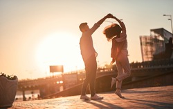 Love is in the air! Cute romantic couple spending time together in the city. Handsome bearded man and attractive young woman are in love. Dancing during sunset.