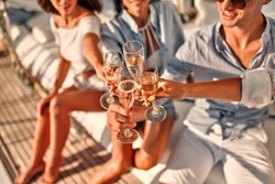 Cheers! Cropped image of group of friends relaxing on luxury yacht and drinking champagne. Having fun together while sailing in the sea. Traveling and yachting concept.
