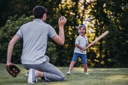 Handsome dad with his little cute sun are playing baseball on green grassy lawn