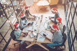 Merry Christmas and Happy New Year 2018!Multiracial young creative people are celebrating holiday in modern office. Group of young business people are sitting in Santa hats in last working day. 