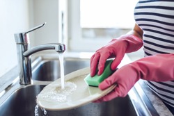 Cropped image of attractive young woman is washing dishes while doing cleaning at home