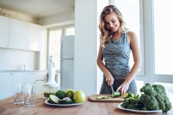 Sporty young woman is preparing healthy food on light kitchen. Green healthy food concept.