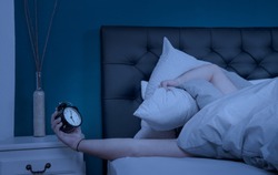 a sleepless man hold his pillow and alarm clock at night