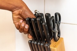 Black woman's hand pulling out a knife from a knife stand. Three black knives of different sizes.
