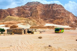 An arid hot desert with mountains and a bus with tourists stopped to eat.