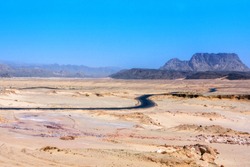 An arid hot desert with mountains and a road under a blue sky.
