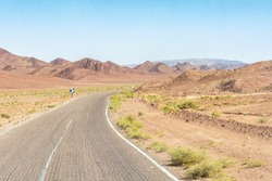 An arid hot desert with mountains and a road under a blue sky.