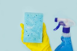 Female hands are holding tools for washing, cleaning, window cleaning products: squeegee, sponge, window cleaning liquid, gloves on a blue background. Cleaning service. copy space.