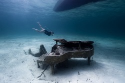 A snorkler swims by an underwater statue of a Mermaid next to a Piano, located in the Bahamas in the Caribbean 