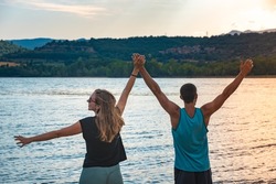 Young Attractive Couple open arms holding hands in a Beautiful Lake in summer during sunset. Discovery Travel love Destination Concept.
