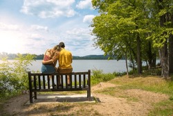 Young loving couple cuddled together on a bench in a lake in summer.