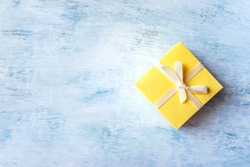 One Yellow gift box with white ribbon and bow on light blue watercolor pastel table background. Minimal festive winter gift background. Top view. Flat lay