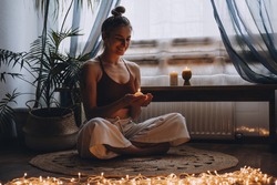 Young woman sitting on the floor, lights candles, enjoy meditation, do yoga exercise at home. Mental health, self care, No stress, healthy habit, mindfulness lifestyle, anxiety relief concept