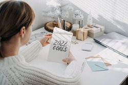 2022 goals, New year resolution. Woman in white sweater writing Text 2022 goals in open notepad on the table. Start new year, planning and setting goals for the next year