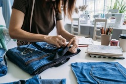 Sustainable fashion, Denim Upcycling Ideas, Using Old Jeans, Repurposing Jeans, Reusing Old Jeans, Upcycle Stuff. Woman seamstress cut and repair old blue jeans in sewing studio.