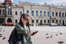 City Summer Vacation, urban trip with audio guide. Audio Tours and Exploring new places. Hipster woman traveler with dreadlocks headphones and cell phone use audio guide and Audio Tours app