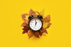 Daylight saving day. Fall Back. Black Alarm clock and autumn leaves on yellow background. Daylight saving time end