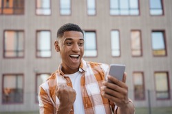 Emotional African American man using mobile phone, shopping online on the street. Happy guy celebration success, sports betting concept	
