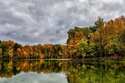 Trees ablaze with the bright colors of fall are reflected in the calm waters of Worster Lake at Potato Creek State Park in North Liberty, Indiana, as ominous storm clouds fill the sky