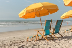 Yellow beach umbrellas with turquoise beach lounge chairs on the sand with ocean bokeh background