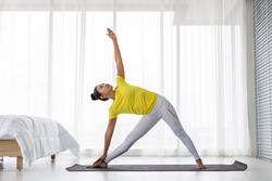 young Asian lady wearing yellow t shirt doing exercise Yoga pose in the bedroom in the morning after woke up.