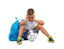 A sad boy isolated on a white background. Tired kid with a bright satchel and a soccer ball. A troubled child. Copy space.