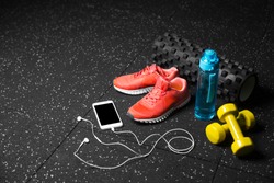 Blue sportive bottle, bright pink training shoes, yellow dumbbells, black pilates mat and smartphone on a black floor background. A colorful set of sportive accessories for gym training. Copy space.