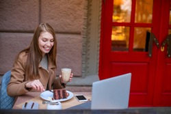 Cheerful girl sitting in a cafe, eating a chocolate dessert and drinking a coffee drink, and smiling. Outside.