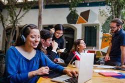 Young latin woman working with computer and her coworkers at the office or coworking in Mexico or South America, Mexican teamwork