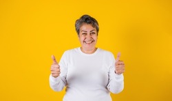 latin matured woman portrait with thumbs up on yellow background in Mexico Latin America
