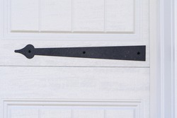 Black powder coated steel spade strap hinge pointing to left on a raised panel white garage door on an American single family house