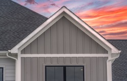White frame gutter guard system, with dark gray horizontal vinyl siding, white accents, fascia, soffit, on a pitched roof attic at a luxury American single family home dramatic colorful sunset sky