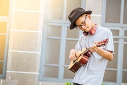 Asian cute boy freedom lifestyle smile practicing playing acoustic guitar music skills on street outdoor background city view have copy space ,Concept of a musician's career concert and young talents 
