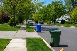 View of a residential tree lined street with green and blue trash bins lined up along the curb for trash truck collection.