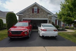 Driveway view of the stone facade of a house with two cars facing in different directions