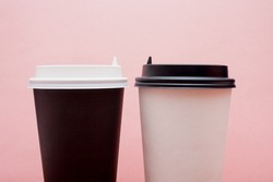 Two different cups of takeaway coffee on a pink background. Issues of segregation and equality of races