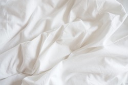 Closeup of beautiful white shiny crumpled polyester fabric sheets on the bed with warm motion and feeling for background and decoration Cloth washing and laundry concept at home