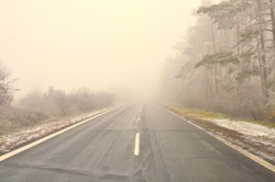 Straight empty wet asphalt road during foggy conditions,glaze ice covered trees, white middle line. Bad weather. 