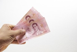 A mans hand is holding three 100 bank notes on a white background. Concept Thai baht currency banknote