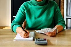 Young Asian housewife doing home income outcome accounts holding receipts from supermarket with calculator, upset by rising grocery prices and surging cost  as an inflation financial crisis.