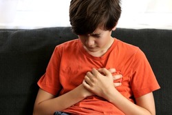 Teenager boy Caucasian holding his chest suffering from pain. Abnormal coronary artery course or origin, or diseases of heart muscle heart attack in children, covid heart concept.