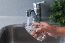 Closeup Woman filling glass with fresh water from faucet in kitchen. Drinking tab water concept.