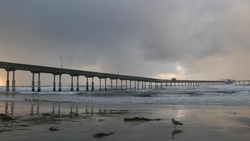 Ocean Beach pier in rainy weather, sea waves in foggy air, California coast, USA. Beachfront boardwalk on piles in water, San Diego. Misty cloudy dramatic shore under pouring downpour. Railfall drops.