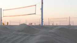 Players playing volleyball on beach court, volley ball game with ball and net, sunset palm trees silhouette, California coast, USA. Defocused people on sandy ocean shore. Seamless looped cinemagraph.